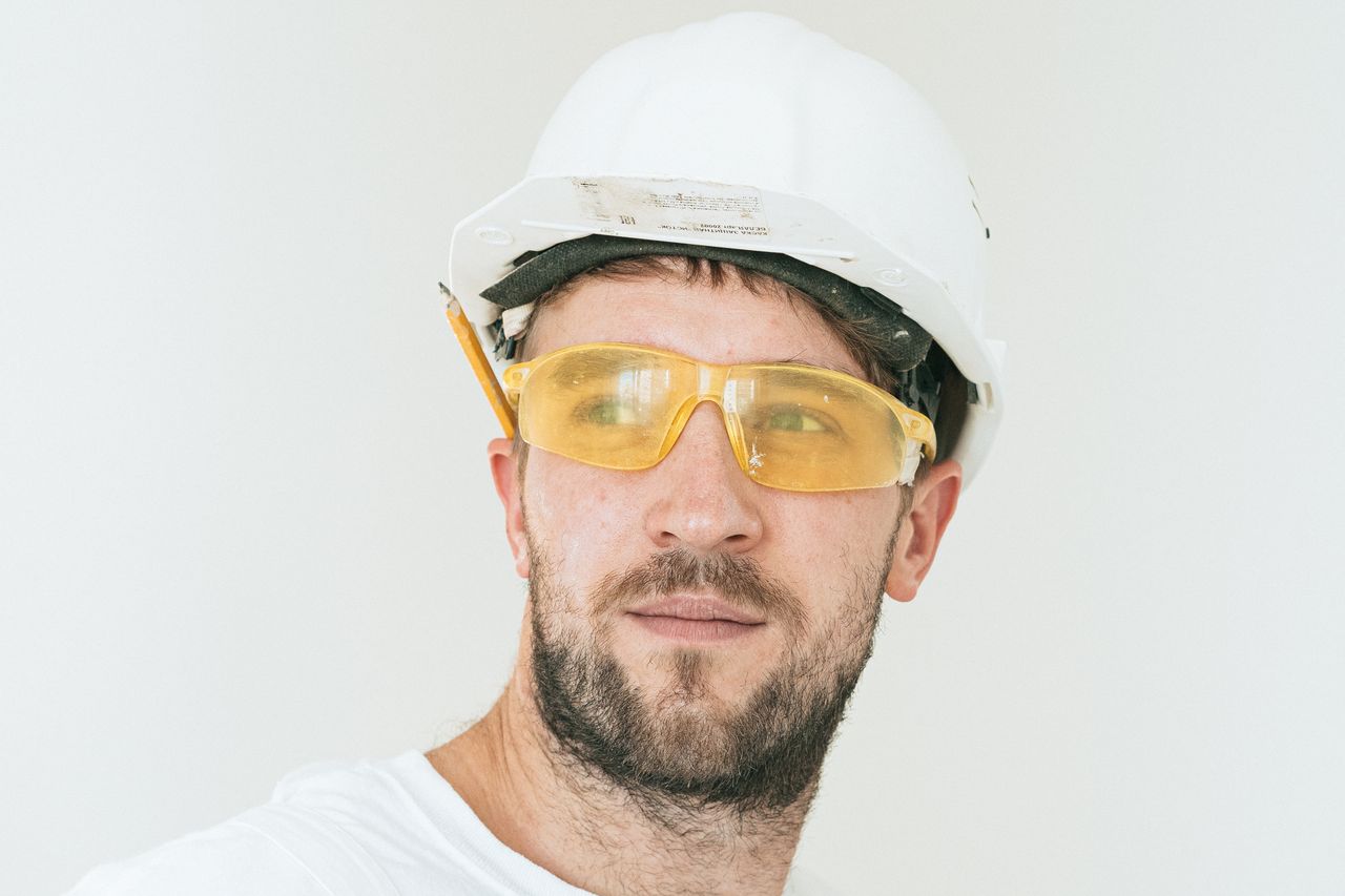 services-img-04 Close-up of a bearded construction worker with safety goggles and hard hat on white background.