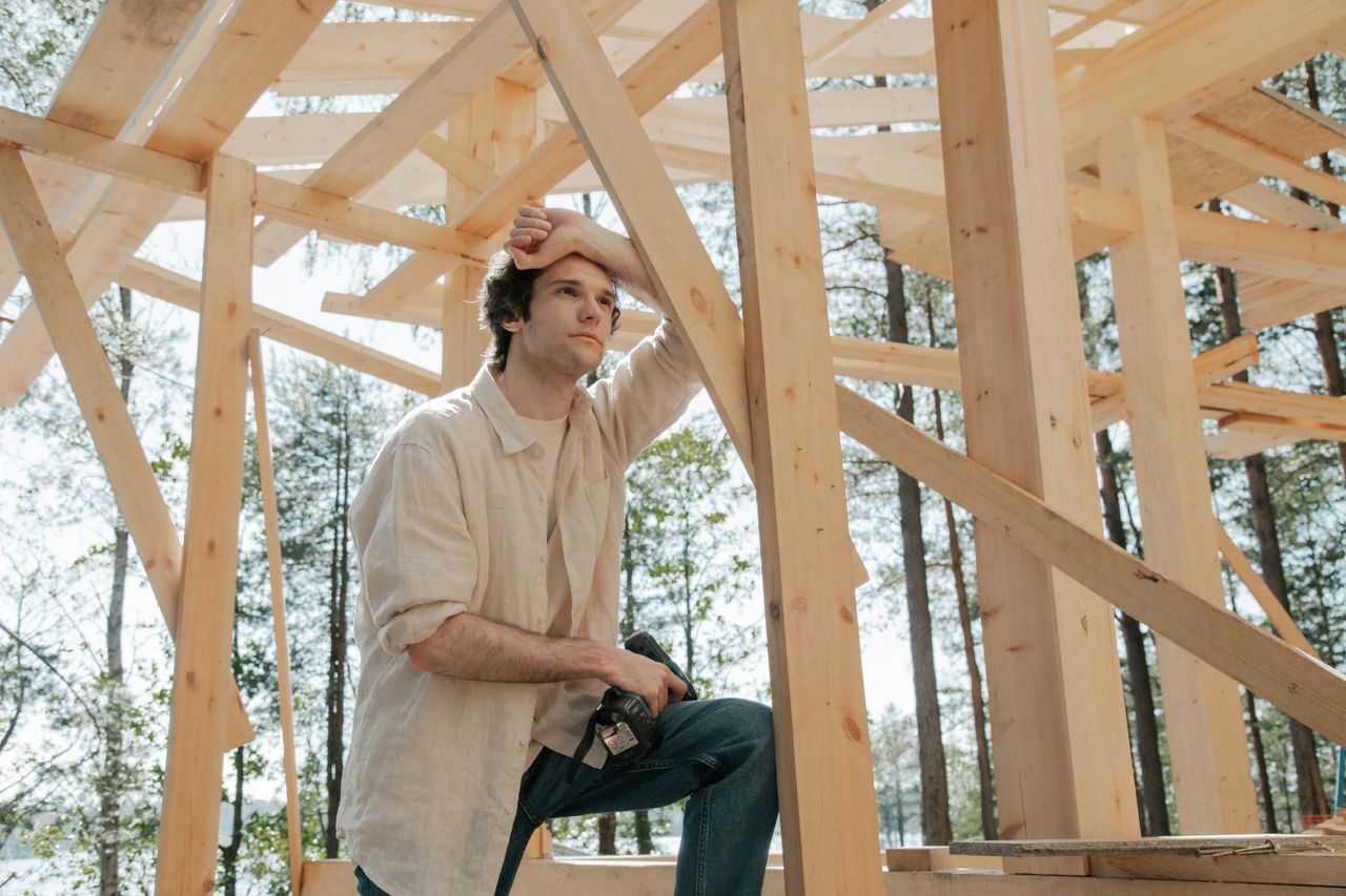 services-img-03 A man in casual attire ponders amidst a wooden structure at a construction site.