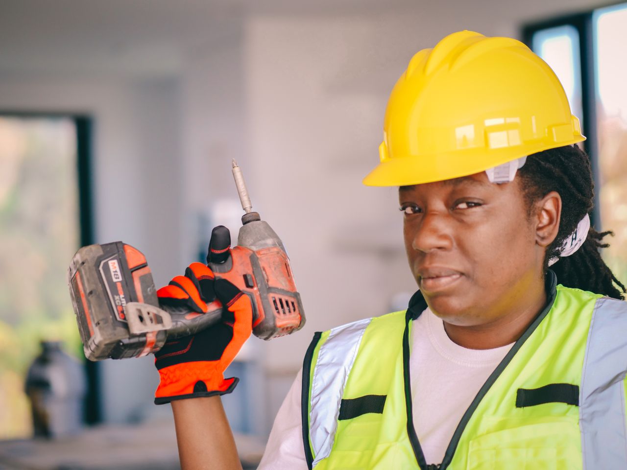 about-us-img Black female construction worker with a drill, wearing safety equipment and hard hat.