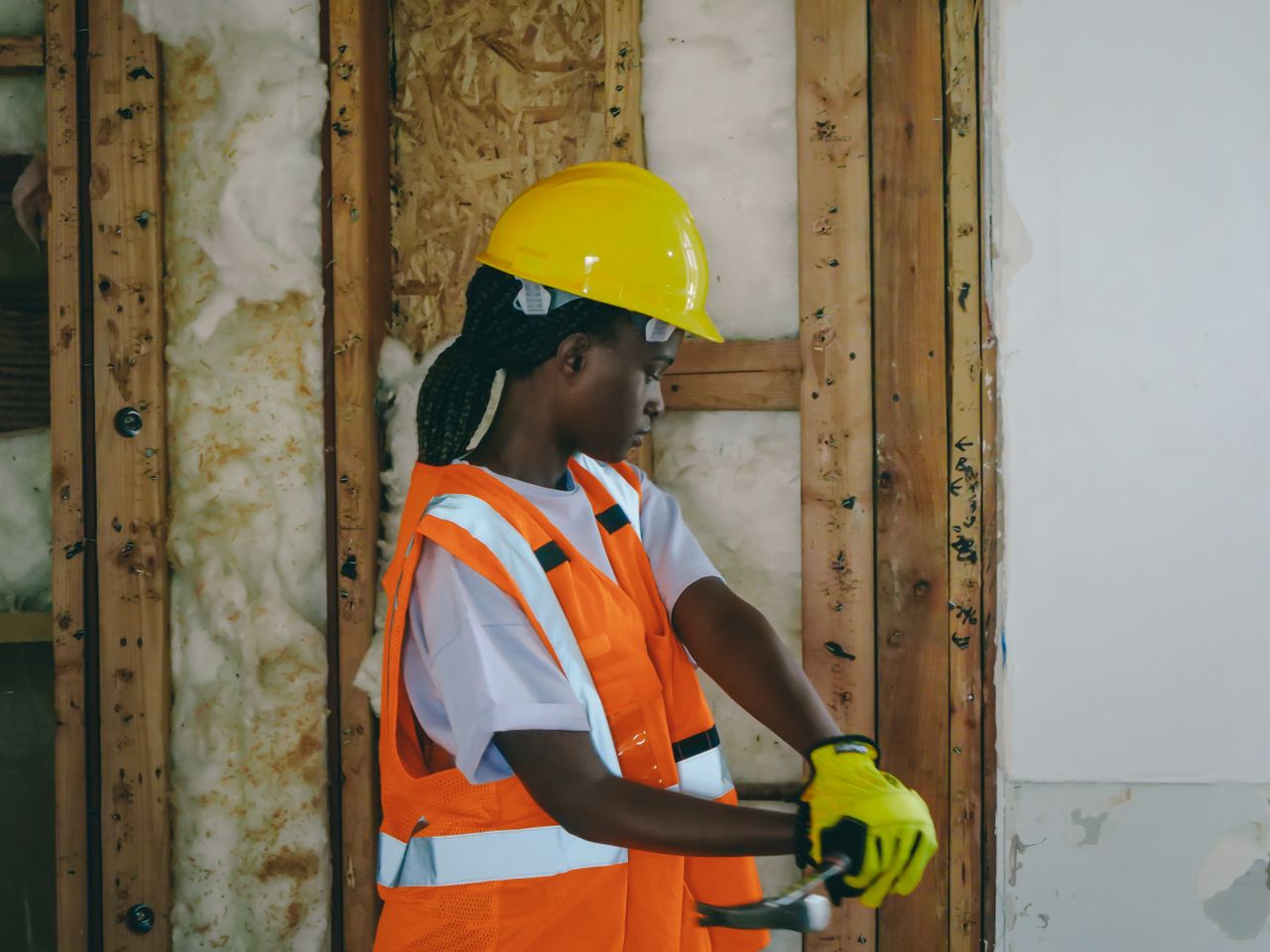our-services-02 Female construction worker in PPE hammering indoors on a renovation site.
