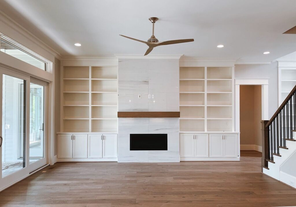 Contemporary living room with built-in shelves, fireplace, and ceiling fan.